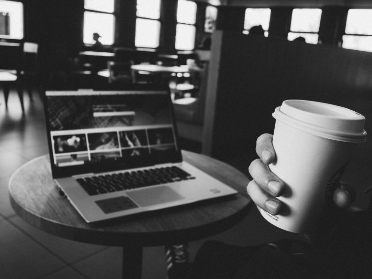 Person Holding Cup Near Powered-on Laptop